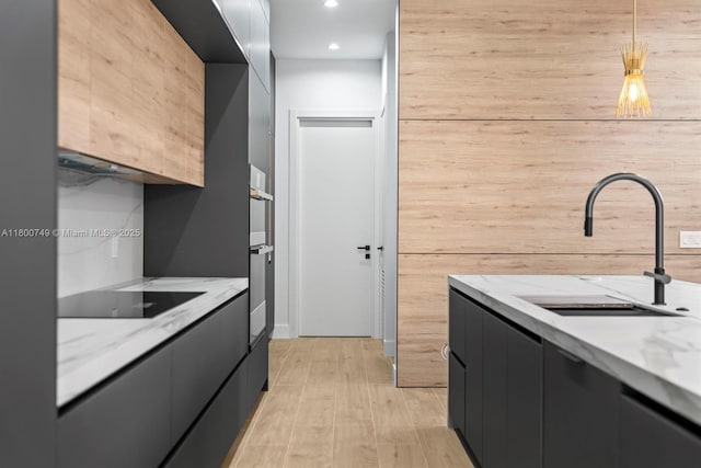 kitchen featuring modern cabinets, black electric stovetop, a sink, dark cabinetry, and light wood-type flooring