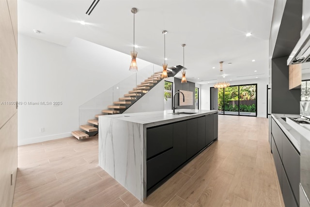 kitchen with modern cabinets, a sink, light wood-style floors, a large island with sink, and dark cabinetry