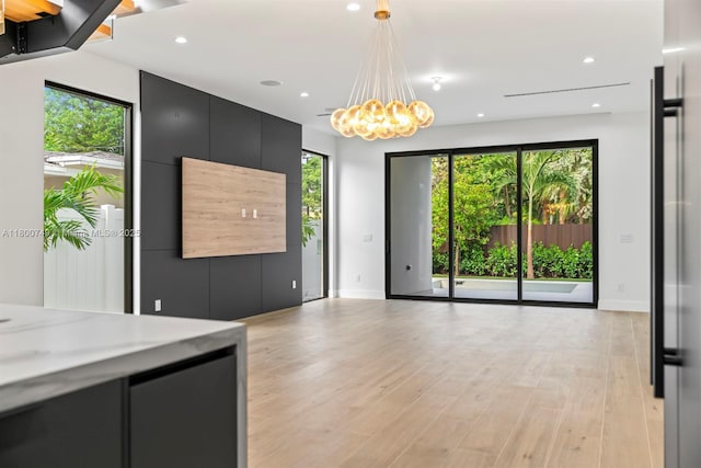 unfurnished living room featuring baseboards, light wood-type flooring, recessed lighting, and a chandelier
