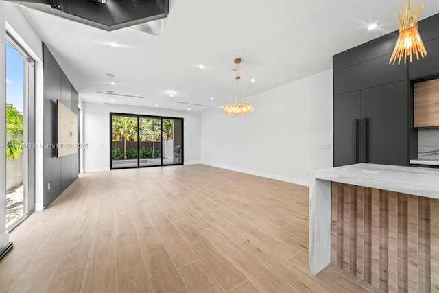 unfurnished living room with light wood finished floors, a chandelier, baseboards, and recessed lighting