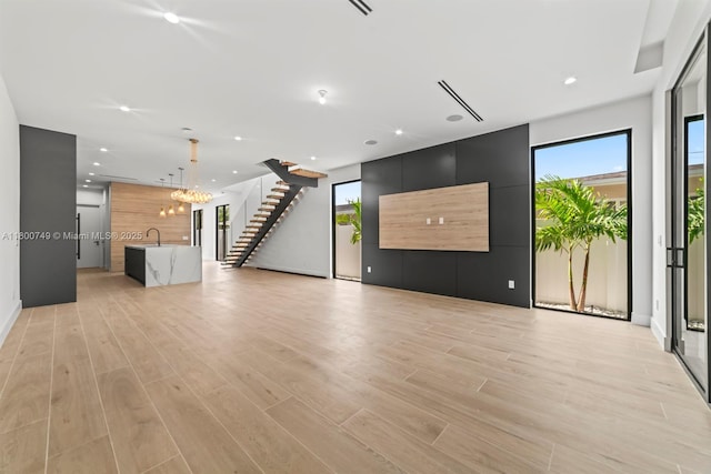 unfurnished living room with light wood-style floors, stairway, a chandelier, recessed lighting, and a sink