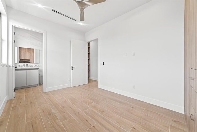 unfurnished bedroom featuring light wood-style flooring, baseboards, and ensuite bathroom