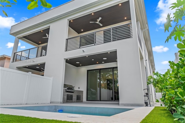 rear view of property with an outdoor kitchen, a balcony, ceiling fan, and stucco siding