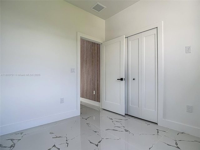 unfurnished bedroom featuring light marble finish floors, baseboards, and a closet