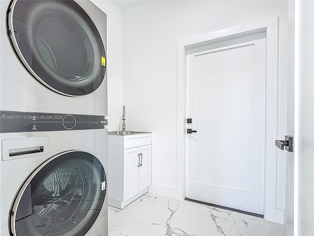 laundry area featuring stacked washing machine and dryer, light marble finish floors, and cabinet space