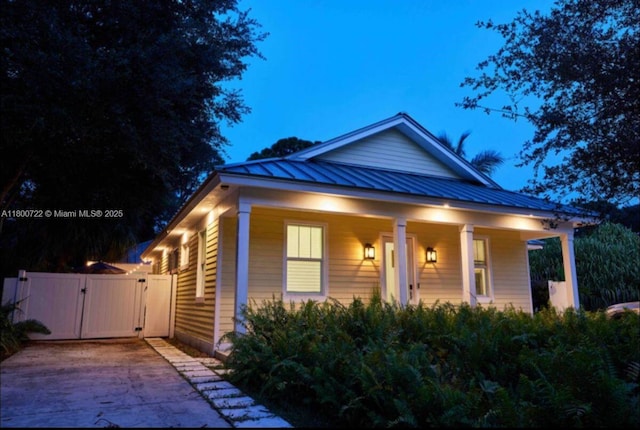view of front of house with a gate, a standing seam roof, covered porch, concrete driveway, and metal roof