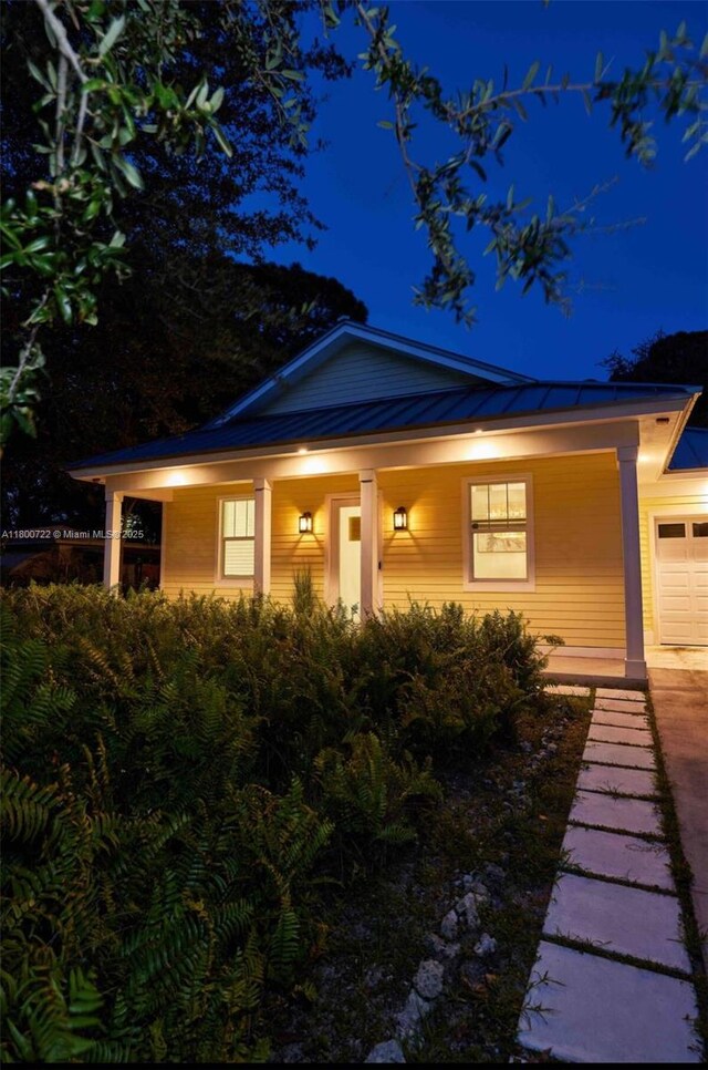 property exterior at night featuring covered porch, a standing seam roof, a garage, metal roof, and concrete driveway