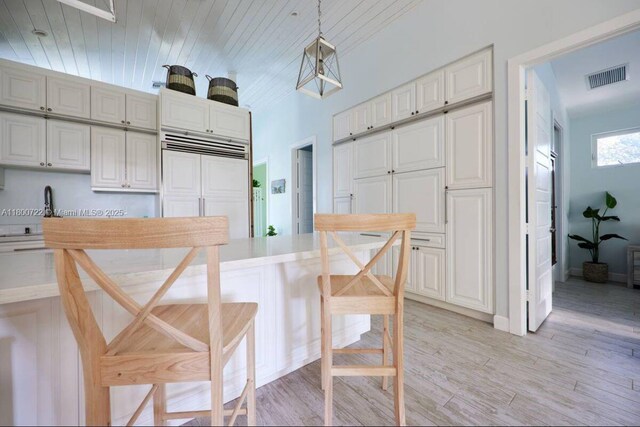 kitchen with paneled refrigerator, light wood-style floors, hanging light fixtures, light countertops, and white cabinetry