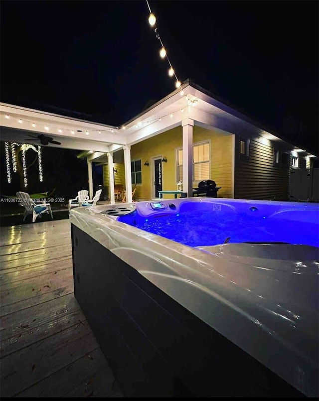pool at night featuring a hot tub, a deck, and ceiling fan
