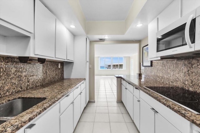 5401 Collins Ave Unit 428, Miami Beach, FL 33140 - kitchen featuring stainless steel microwave, black electric stovetop, light tile patterned floors, white cabinets, and tasteful backsplash