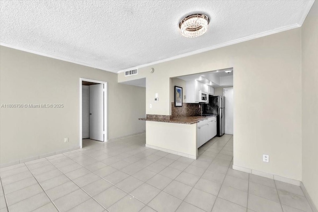 5401 Collins Ave Unit 428, Miami Beach, FL 33140 - kitchen featuring white microwave, crown molding, a textured ceiling, freestanding refrigerator, and white cabinetry