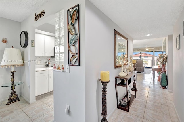 hallway with a textured ceiling, baseboards, and light tile patterned floors