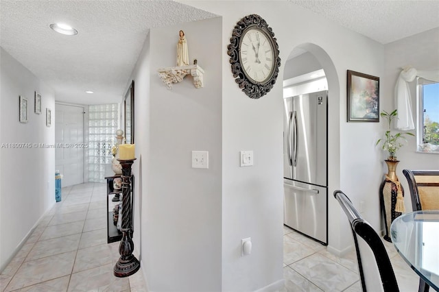 corridor with a textured ceiling, arched walkways, light tile patterned floors, and baseboards