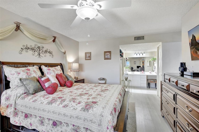 bedroom featuring a textured ceiling, light wood-type flooring, ensuite bath, and a ceiling fan
