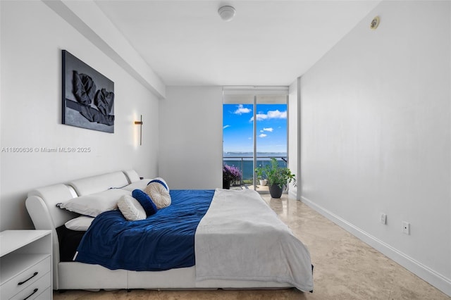 bedroom with a wall of windows, a water view, and baseboards