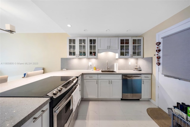 kitchen with appliances with stainless steel finishes, light marble finish flooring, a sink, decorative backsplash, and glass insert cabinets
