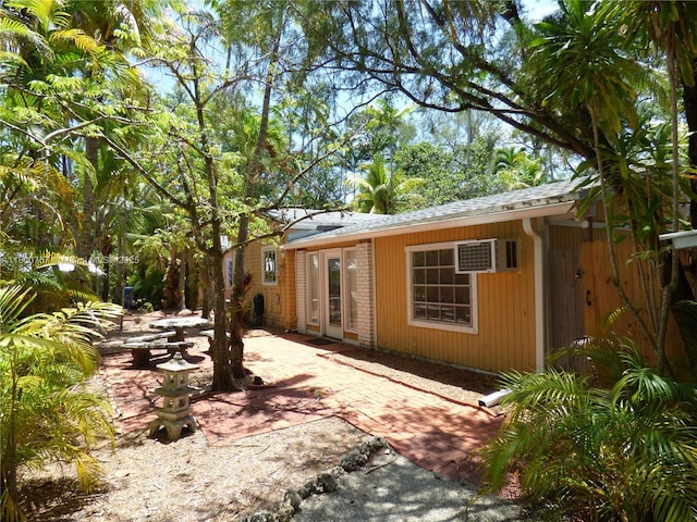 view of property exterior with a patio area, a wall mounted air conditioner, and roof with shingles