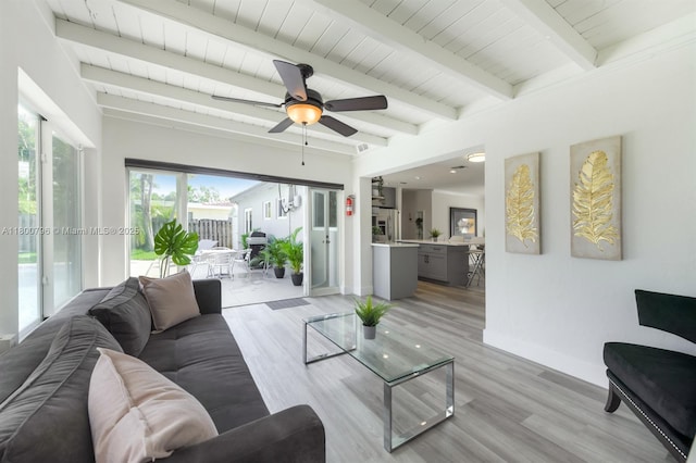 living area featuring beamed ceiling, a ceiling fan, light wood-style flooring, and baseboards