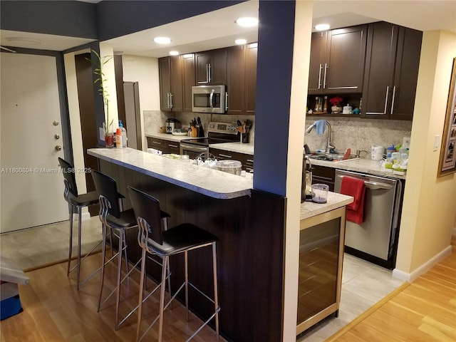 kitchen featuring appliances with stainless steel finishes, wine cooler, a kitchen bar, tasteful backsplash, and dark brown cabinets