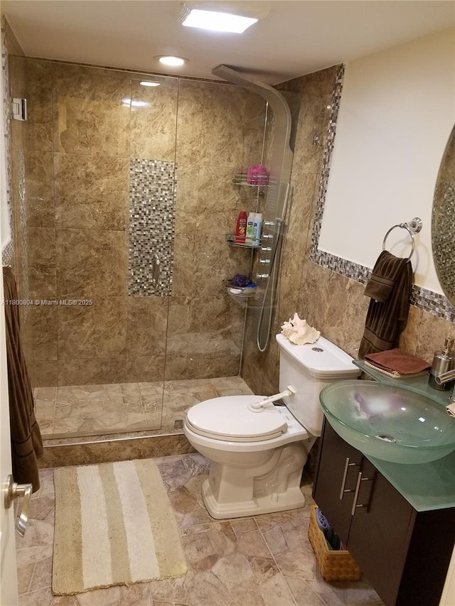 full bath with toilet, tiled shower, tile walls, and vanity
