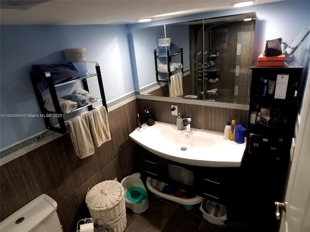 bathroom featuring a wainscoted wall, toilet, a sink, tile patterned floors, and a shower
