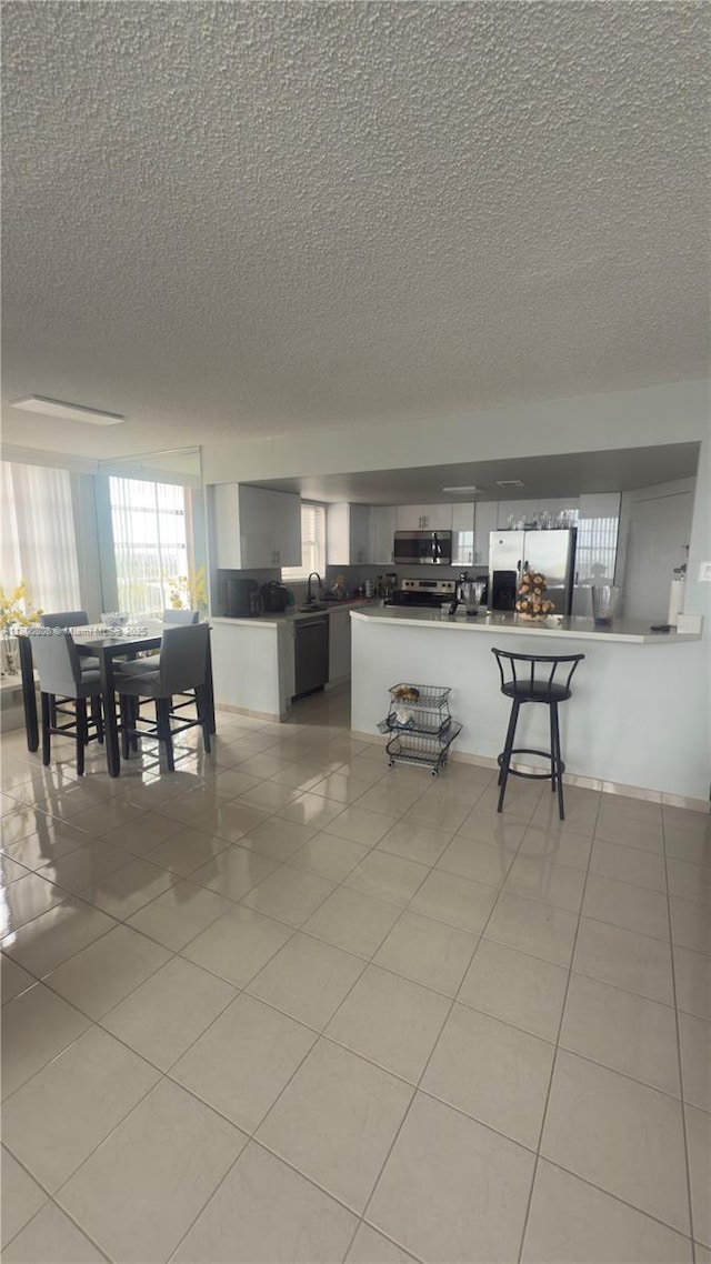 1351 NE Miami Gardens Dr Unit 1225E, Miami, FL 33179 - kitchen with appliances with stainless steel finishes, a textured ceiling, light tile patterned flooring, a peninsula, and a kitchen bar