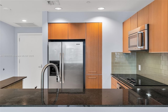1060 Brickell Ave Unit 1811, Miami, FL 33131 - kitchen featuring stainless steel appliances, dark stone counters, backsplash, brown cabinets, and a peninsula