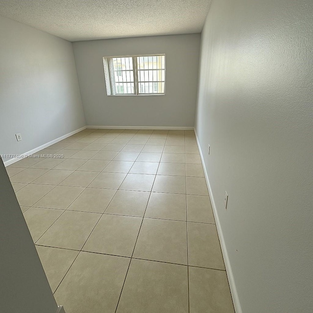 empty room featuring light tile patterned floors, a textured ceiling, and baseboards