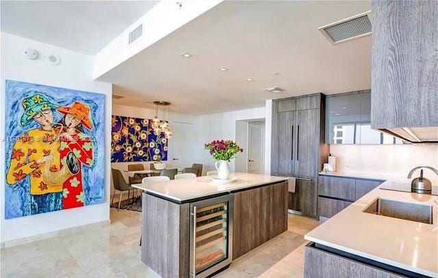 kitchen featuring modern cabinets, beverage cooler, a kitchen island, a sink, and light countertops