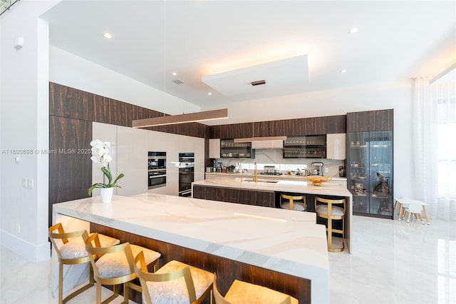9625 Vescovato Way, Boca Raton, FL 33496 - kitchen featuring modern cabinets, a large island, a kitchen bar, light stone counters, and a sink
