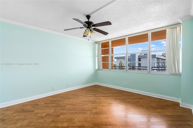 spare room with a textured ceiling, crown molding, a ceiling fan, wood finished floors, and baseboards