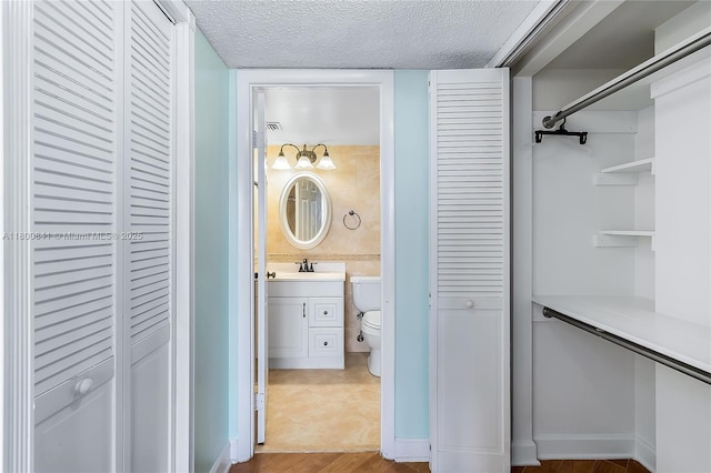 bathroom with a closet, vanity, toilet, and a textured ceiling