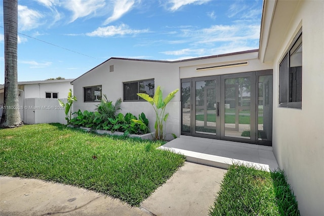 129 NE 2nd Ave, Dania Beach, FL 33004 - view of exterior entry featuring stucco siding, french doors, and a lawn