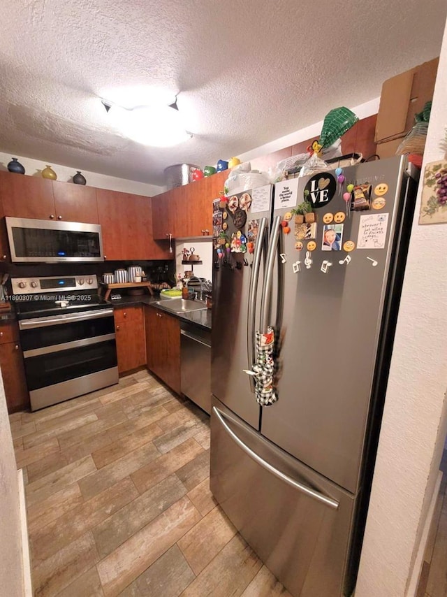 kitchen featuring stainless steel appliances, dark countertops, brown cabinets, a sink, and a textured ceiling