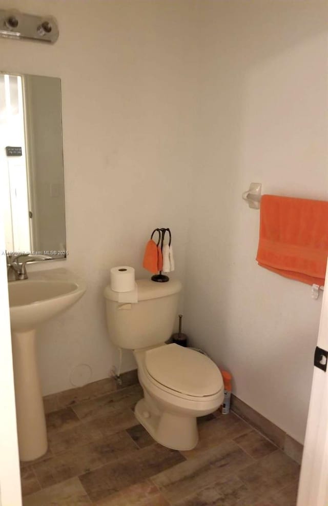 half bathroom featuring toilet, wood finished floors, and a sink