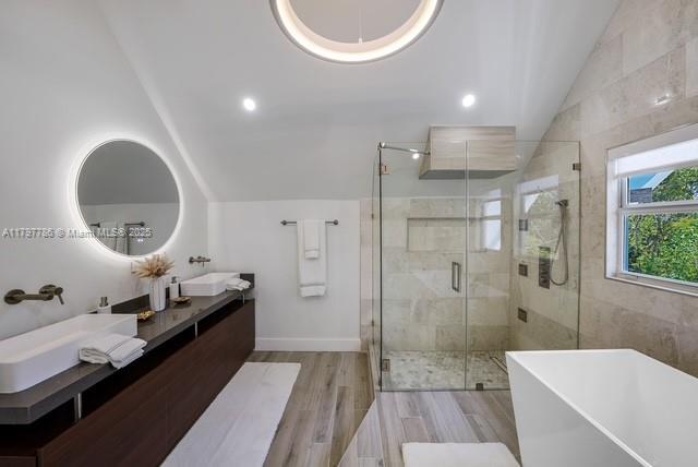 bathroom with lofted ceiling, a stall shower, wood finished floors, a soaking tub, and double vanity