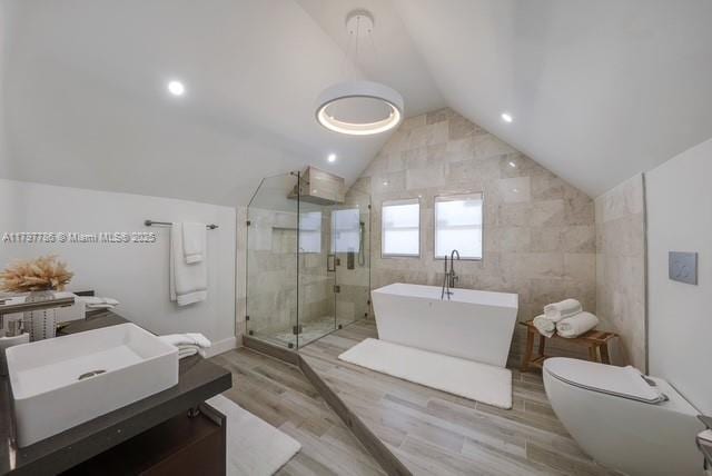bathroom featuring vaulted ceiling, wood finished floors, a shower stall, a soaking tub, and toilet