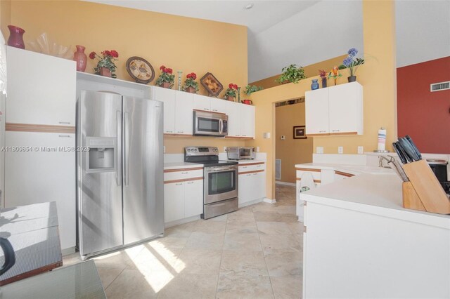 kitchen with stainless steel appliances, high vaulted ceiling, light countertops, white cabinets, and a peninsula