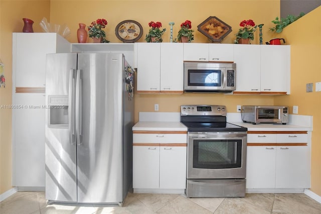 kitchen with appliances with stainless steel finishes, light countertops, white cabinetry, light tile patterned floors, and baseboards