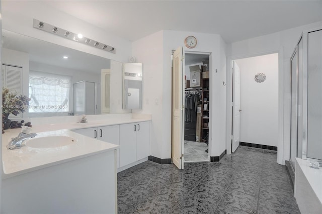 bathroom with a shower stall, baseboards, vanity, and a spacious closet