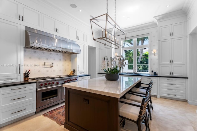 kitchen with premium stove, a chandelier, under cabinet range hood, tasteful backsplash, and ornamental molding