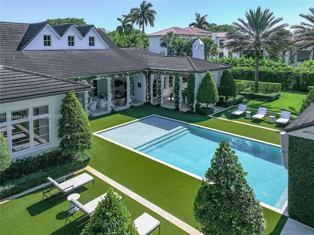 back of property featuring a patio area, a lawn, an outdoor pool, and a tiled roof