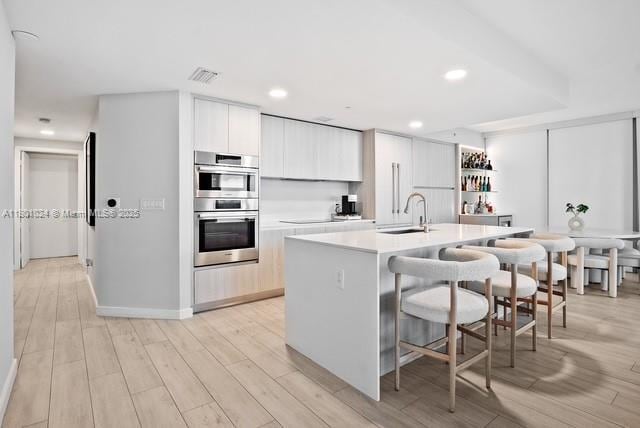 488 NE 18th St Unit 715, Miami, FL 33132 - kitchen featuring a sink, stainless steel double oven, a kitchen bar, light countertops, and a center island with sink