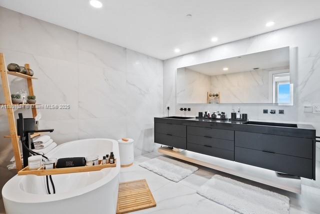 488 NE 18th St Unit 715, Miami, FL 33132 - full bathroom featuring double vanity, a freestanding tub, recessed lighting, and tile walls
