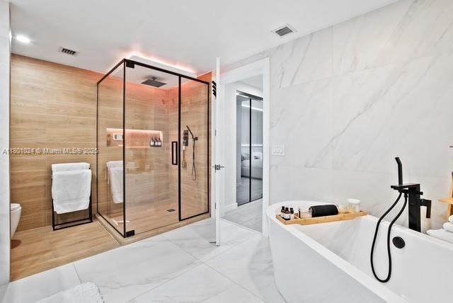 488 NE 18th St Unit 715, Miami, FL 33132 - bathroom featuring tile walls, a shower stall, a freestanding tub, marble finish floors, and toilet