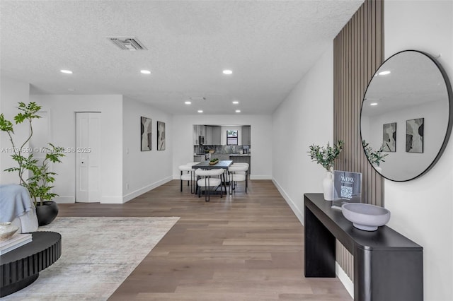 corridor with recessed lighting, wood finished floors, baseboards, and a textured ceiling
