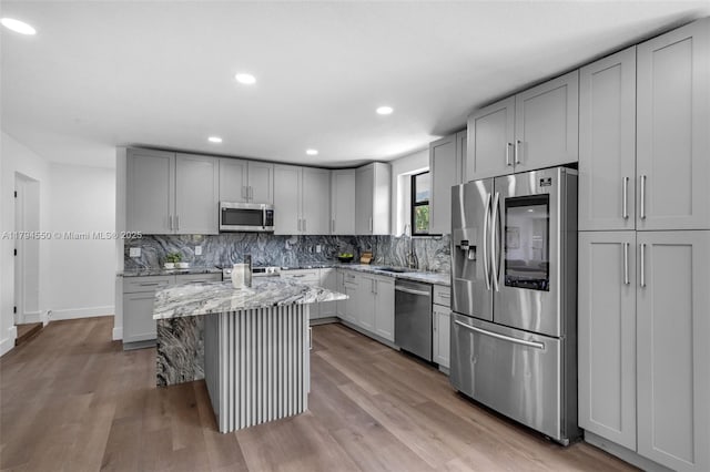 kitchen with stainless steel appliances, gray cabinetry, light stone countertops, a kitchen island, and decorative backsplash