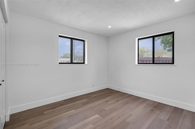 unfurnished room with recessed lighting, wood finished floors, baseboards, and a textured ceiling