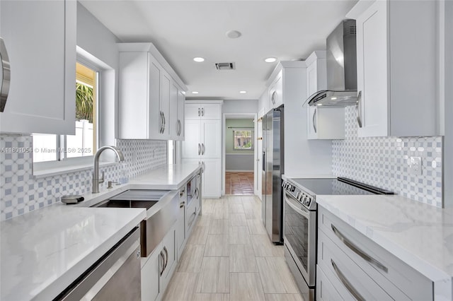 5261 NE 18th Ter, Fort Lauderdale, FL 33308 - kitchen with wall chimney range hood, stainless steel appliances, a sink, white cabinets, and light stone counters