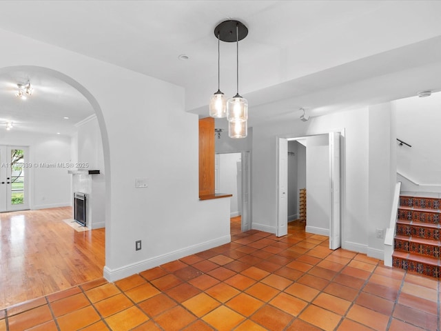 1125 Asturia Ave, Coral Gables, FL 33134 - empty room with stairway, arched walkways, light tile patterned floors, a fireplace with flush hearth, and baseboards